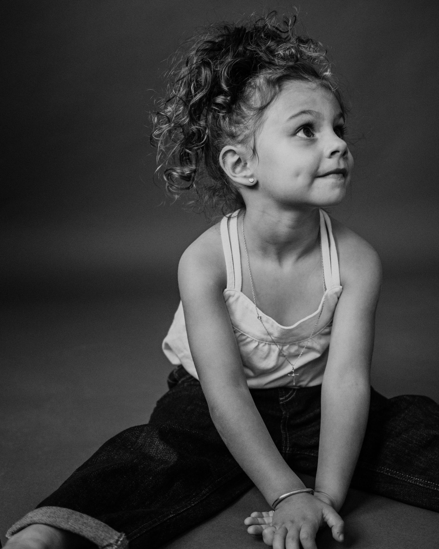 Black and white portrait of child in tank top sitting with curly hair.