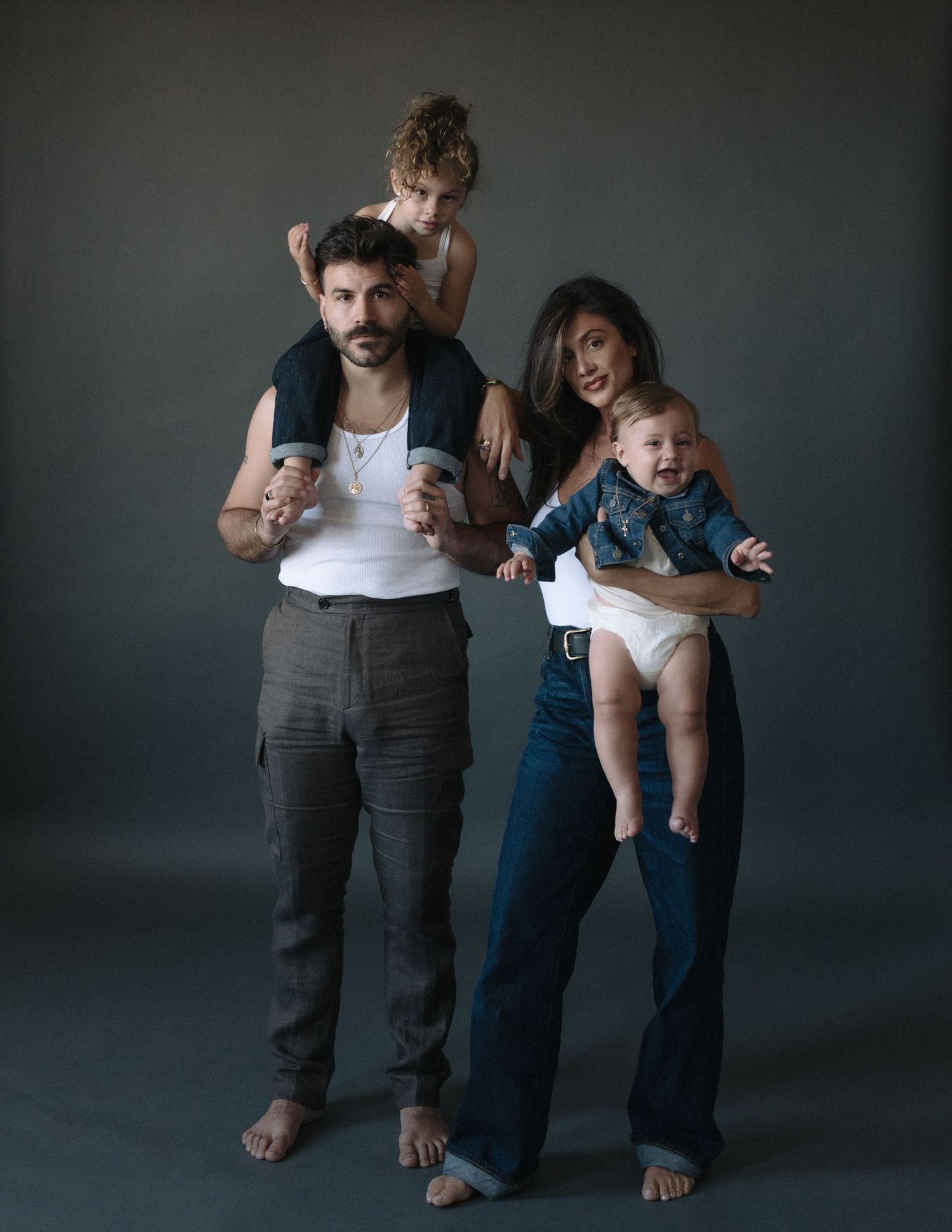 Studio portrait of family with two children in casual attire against dark background.