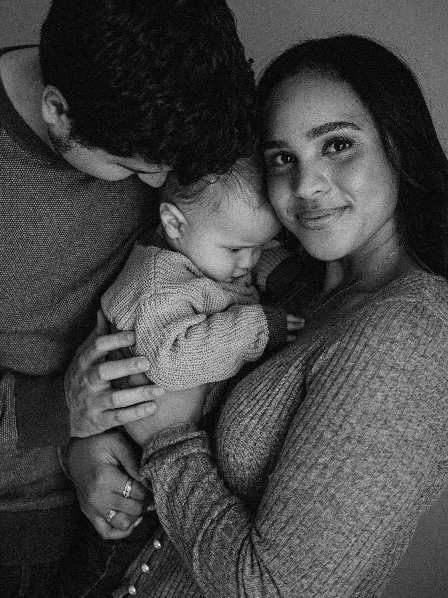 An intimate black and white family portrait showing tender moments with a baby.