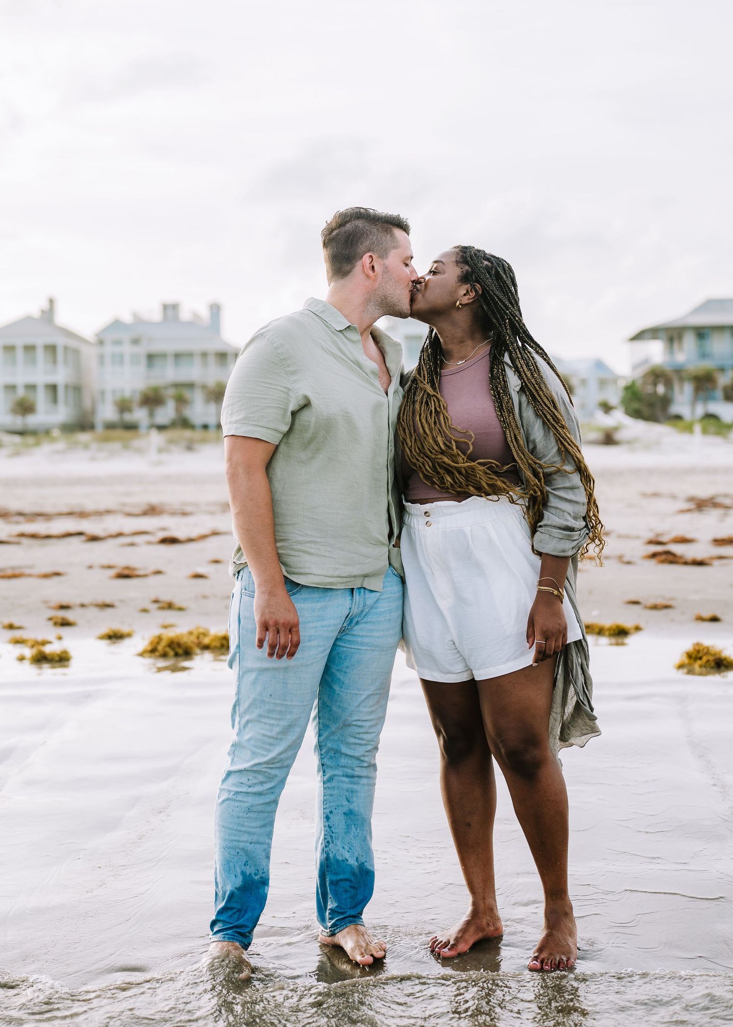 Intimate beach portrait session with couple standing in shallow ocean water at sunset.