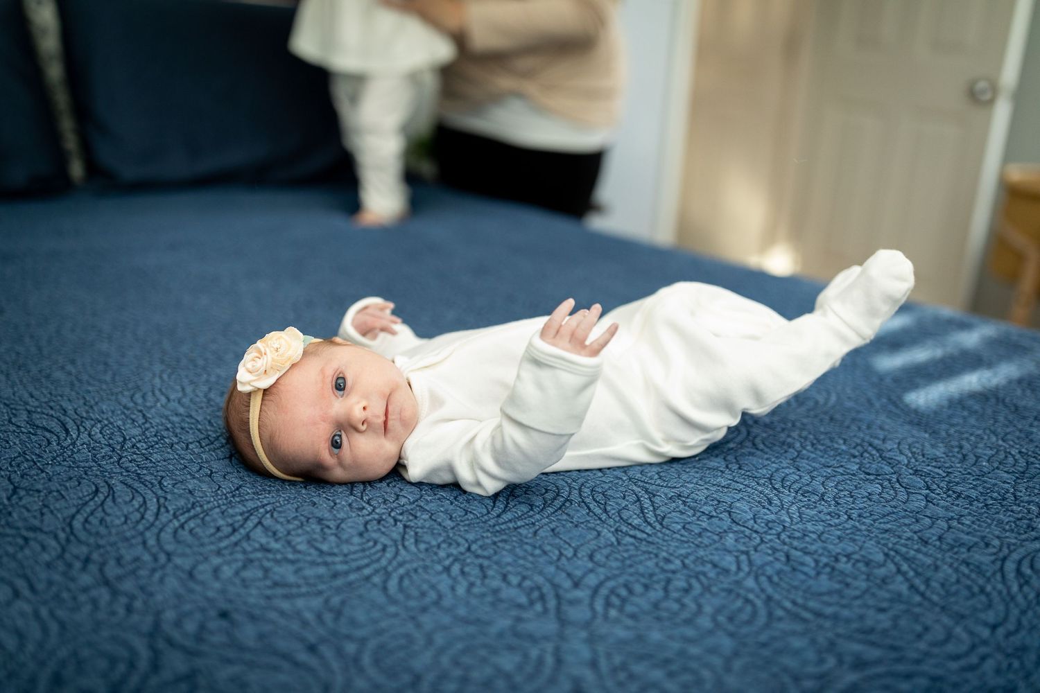 A smiling baby in white clothing lies on a blue textured bedspread.