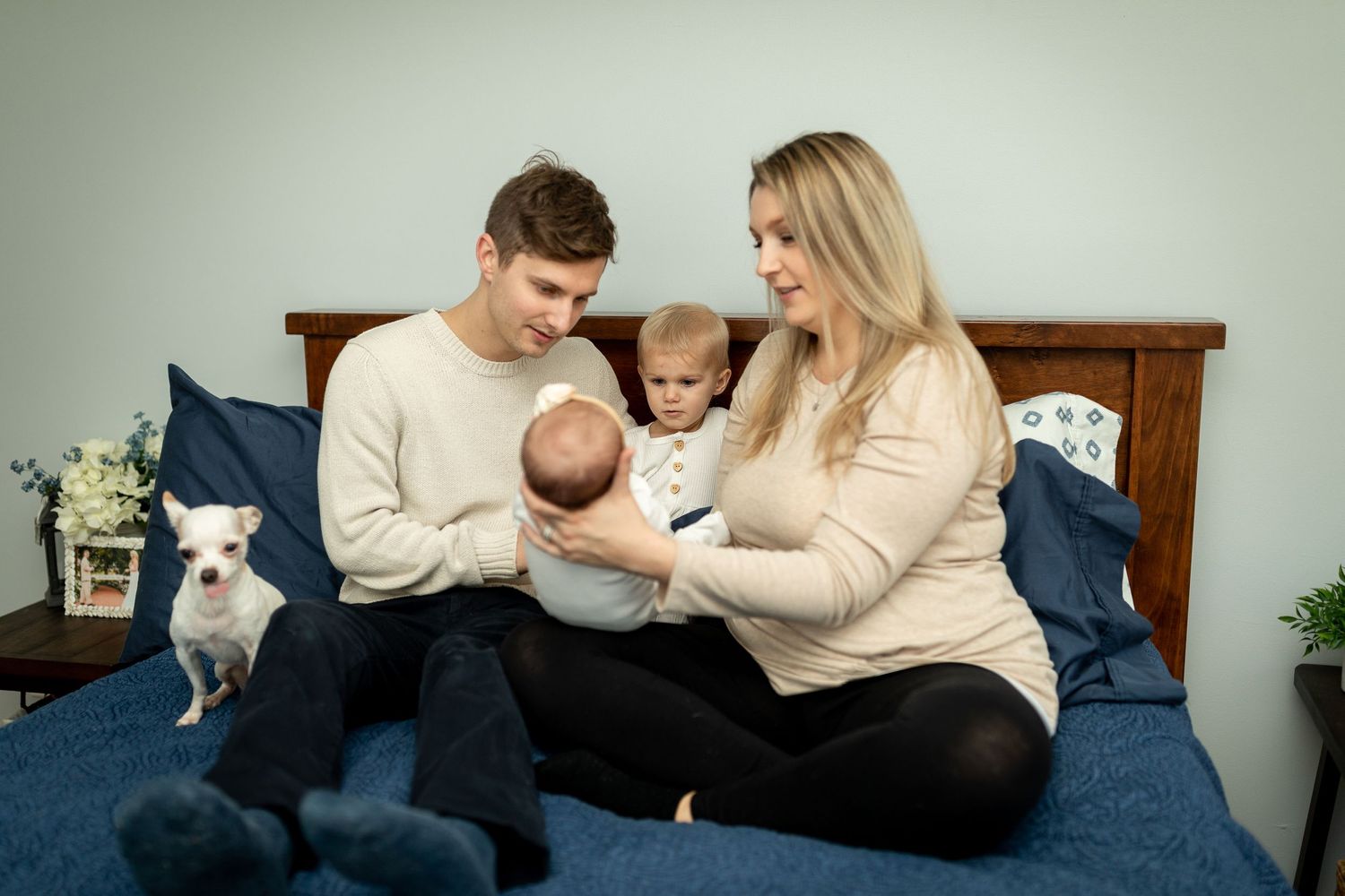 A family shares a cozy moment on a blue bed with their small white dog nearby.