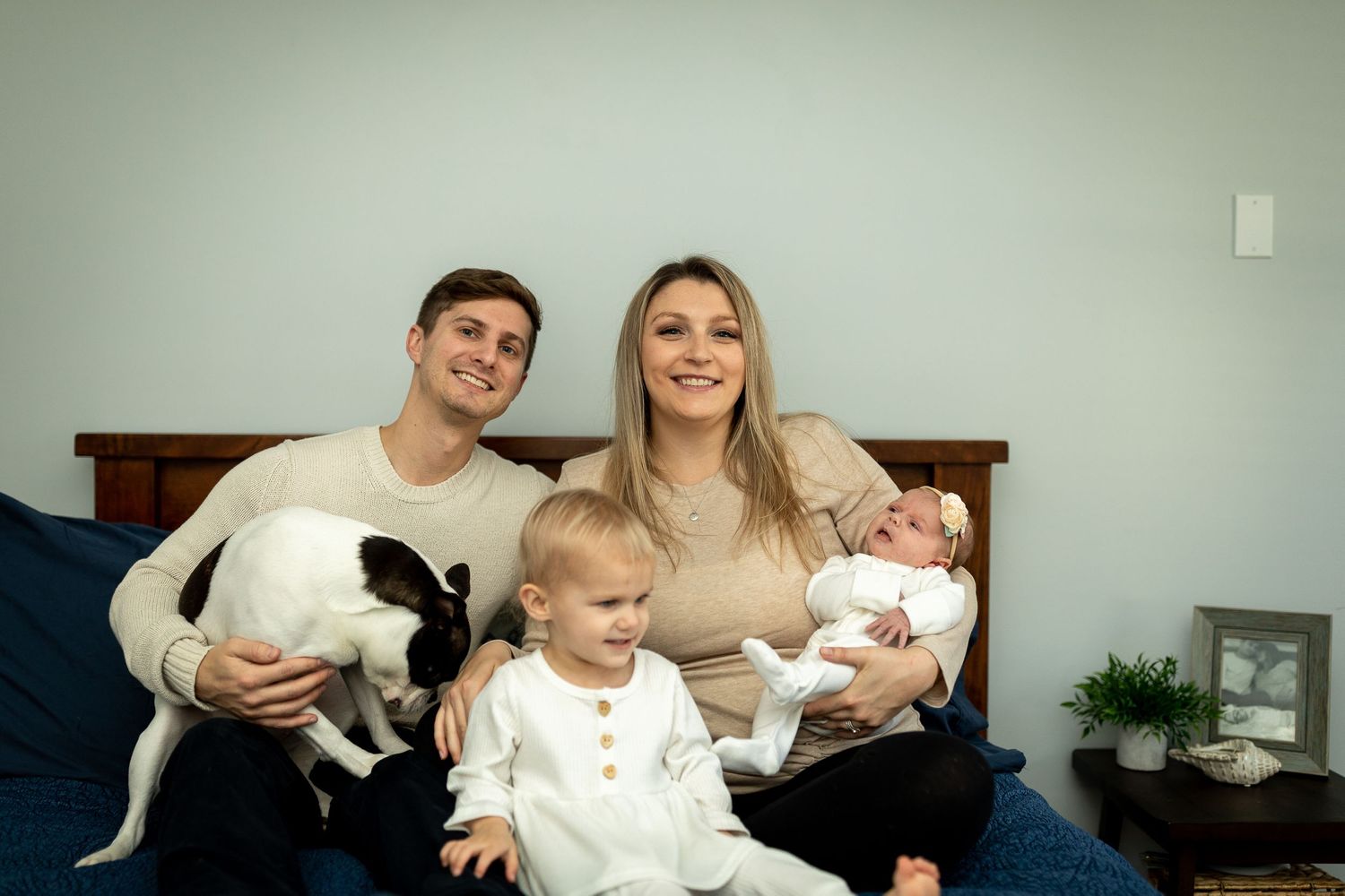 A family poses together on their bed with their black and white dog and children.