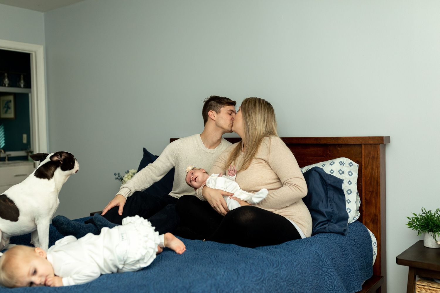 A family shares intimate moments together on a blue bed with their spotted dog.