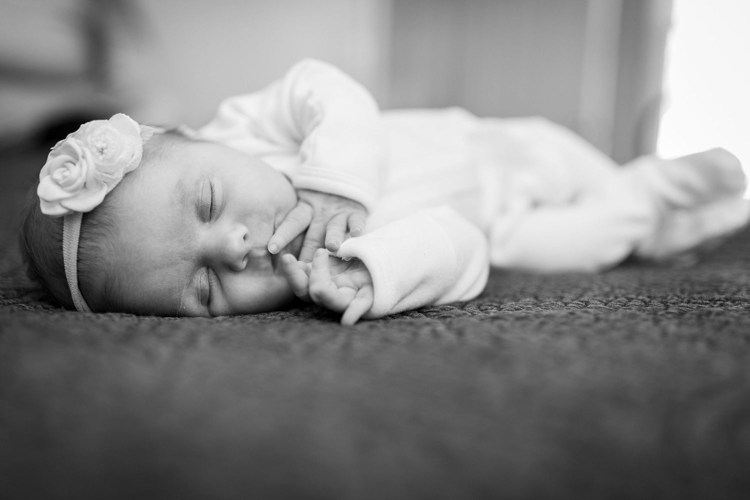 Black and white portrait of a sleeping infant lying on carpet wearing a floral headband.