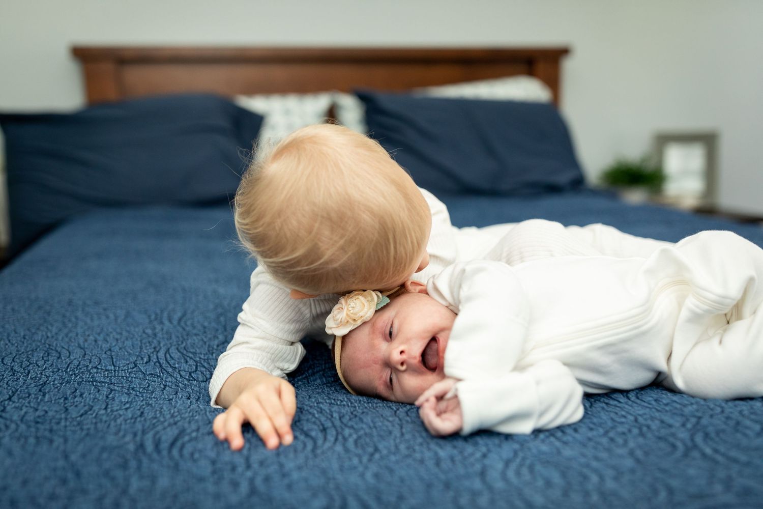 Baby in cozy white outfit lying on navy blue bedspread.