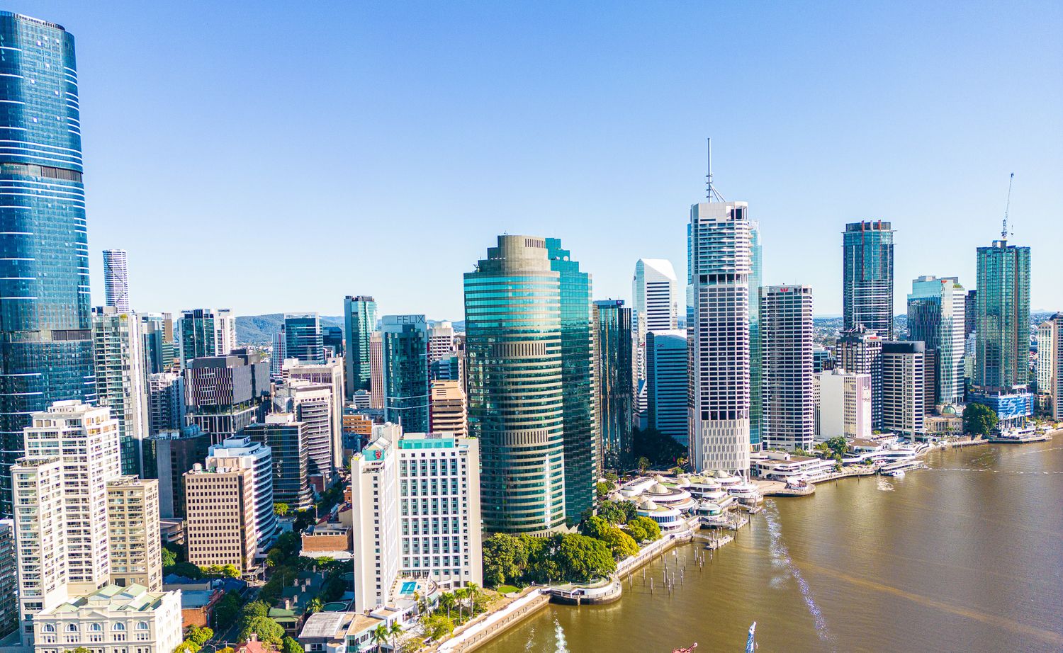 Modern Brisbane city skyline with tall glass buildings along the river under clear blue skies.