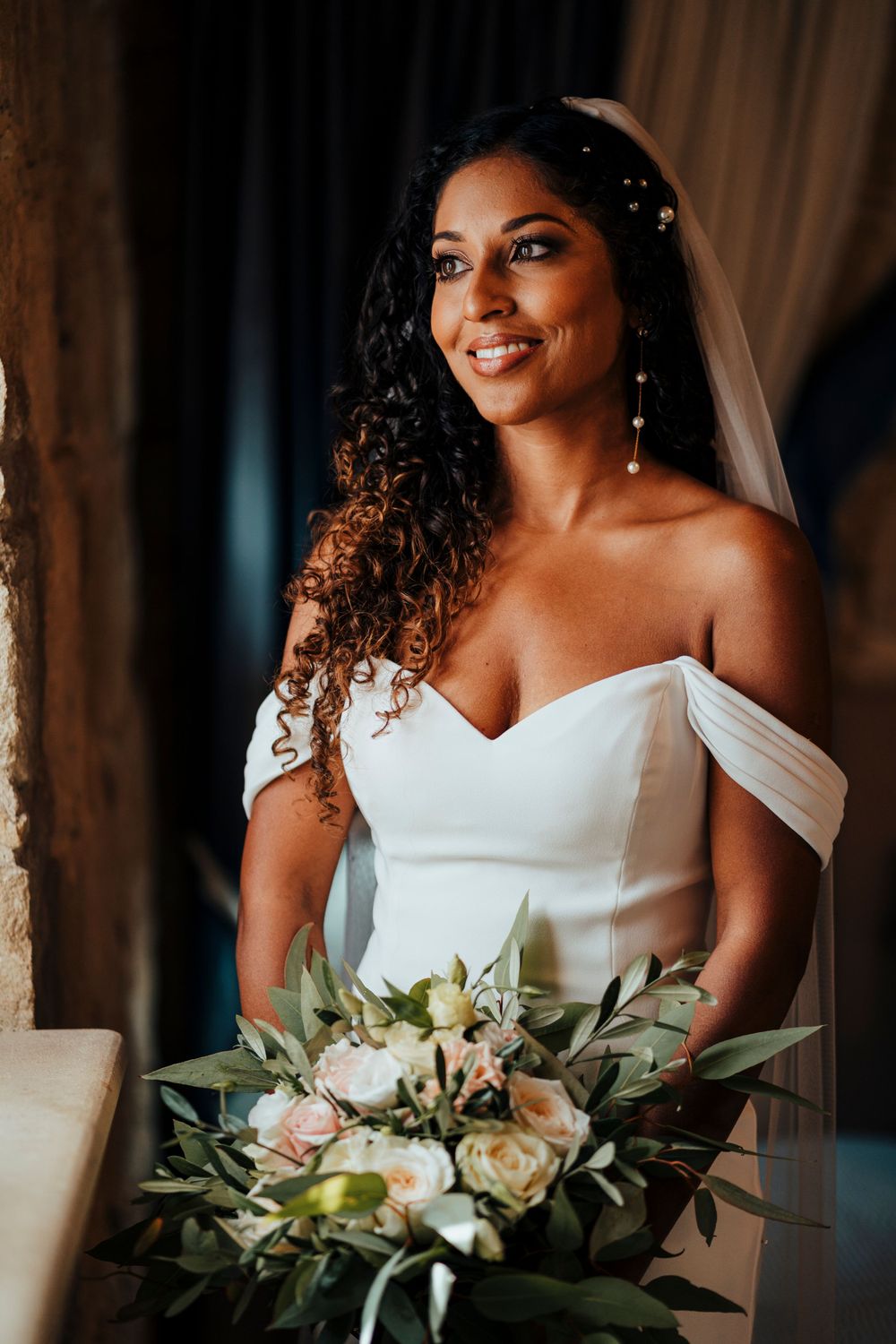 Radiant bride poses with white and green bouquet in elegant off-shoulder wedding gown.