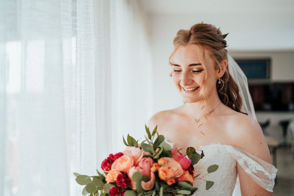 A bride smiles while holding a colorful bouquet of roses and greenery.