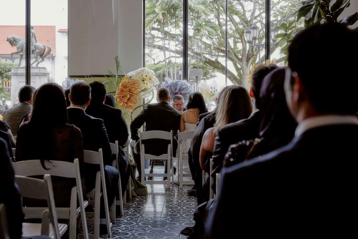 Wedding ceremony setup with white chairs and floral decorations in a bright indoor venue.