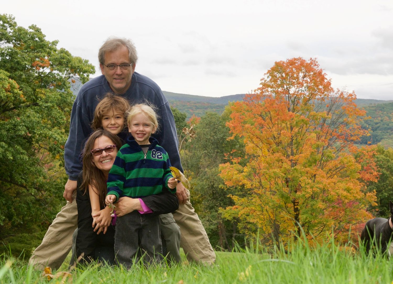 Family poses together on grassy hill with vibrant fall foliage in background.