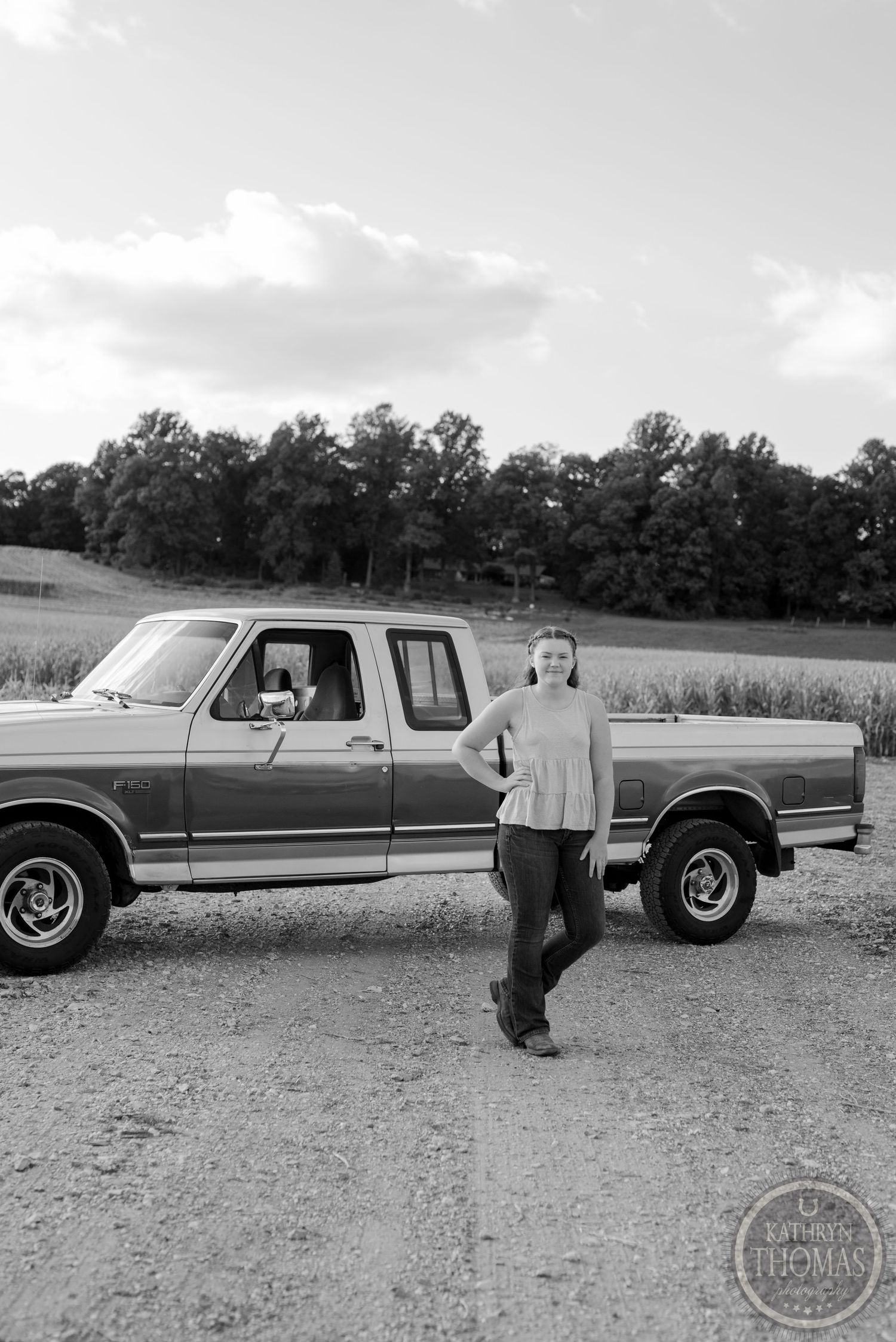 Classic Ford pickup truck shown in black and white photography on a country road by agricultural fields.