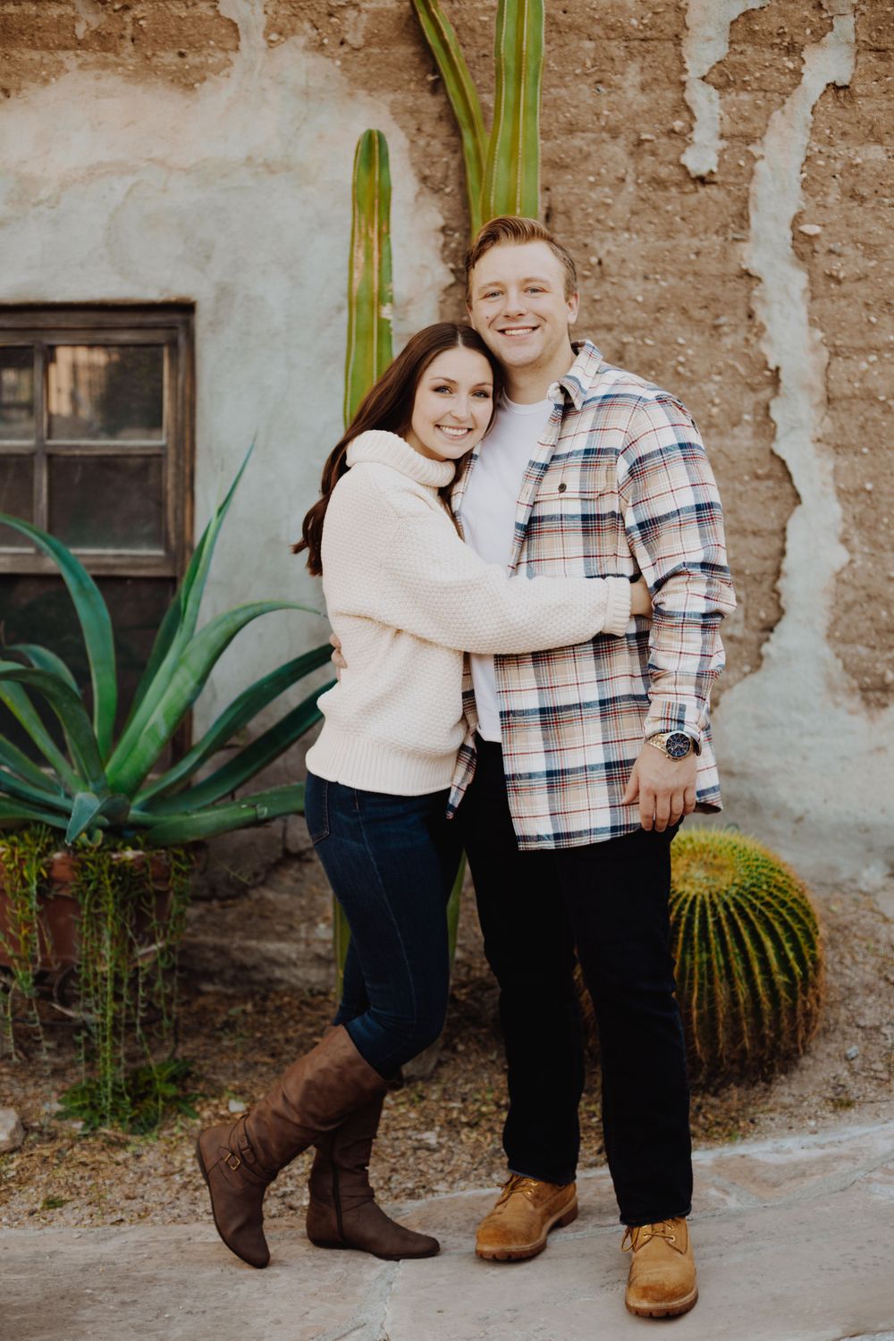 Casual couple photos against weathered adobe wall with desert plants.