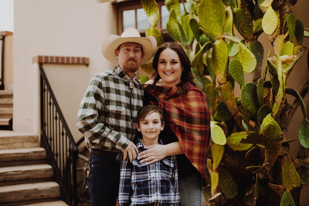 Family poses together in front of a southwestern style building with cactus plants.