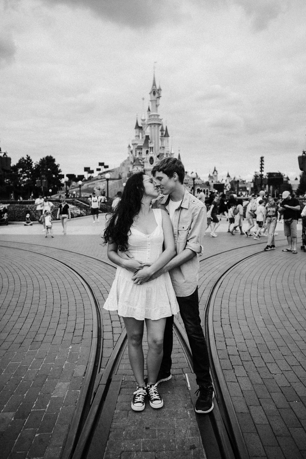 Black and white photo of couple sharing a romantic moment in front of Disneyland Paris castle.
