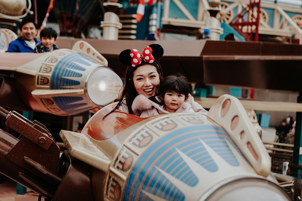 Smiling mother and young daughter enjoying a rocket ride attraction at Disneyland wearing Minnie ears.