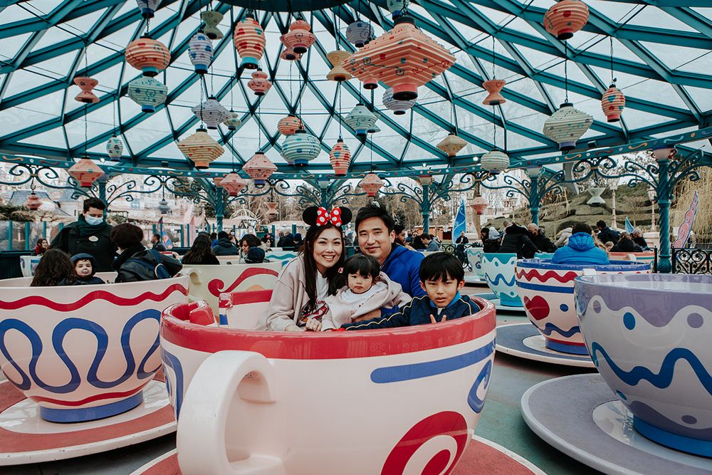 Happy Asian family sitting in a teacup ride under colorful decorations at Disneyland Paris.