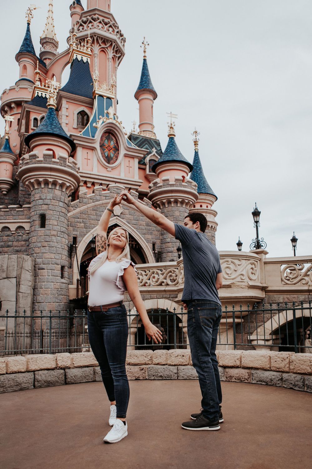 Joyful couple dancing and spinning in front of Sleeping Beauty Castle at Disneyland Paris.