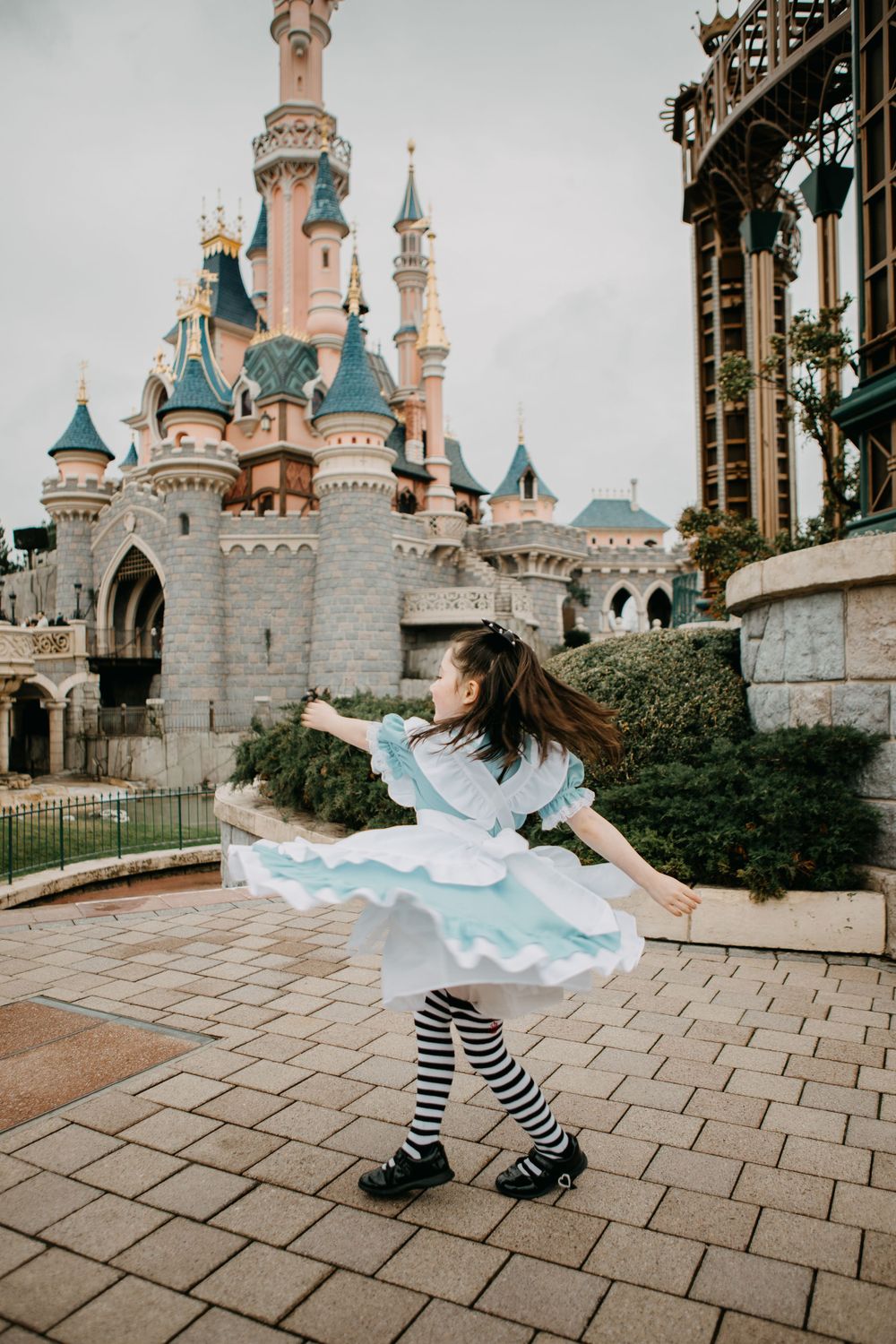 Girl in Alice in Wonderland costume twirling in front of Sleeping Beauty Castle at Disneyland Paris.