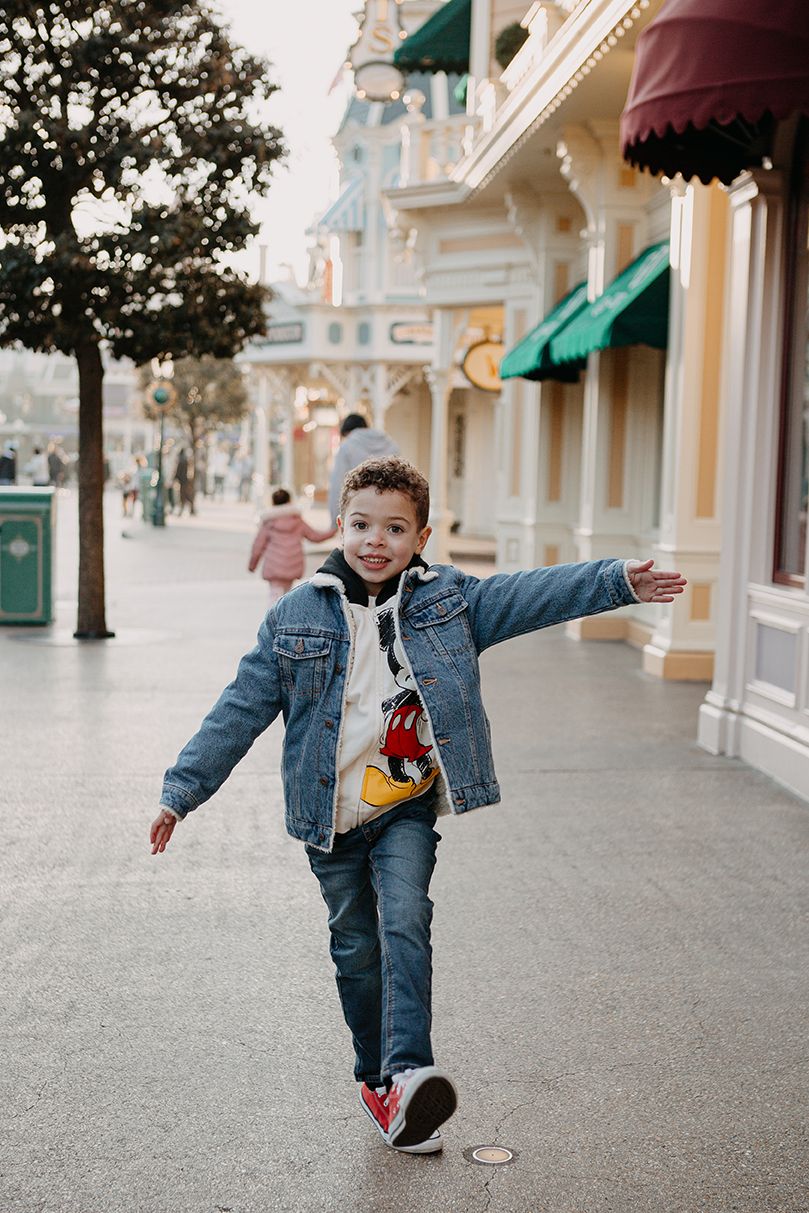 Joyful young boy runs with arms outstretched along Main Street at Disneyland Paris.