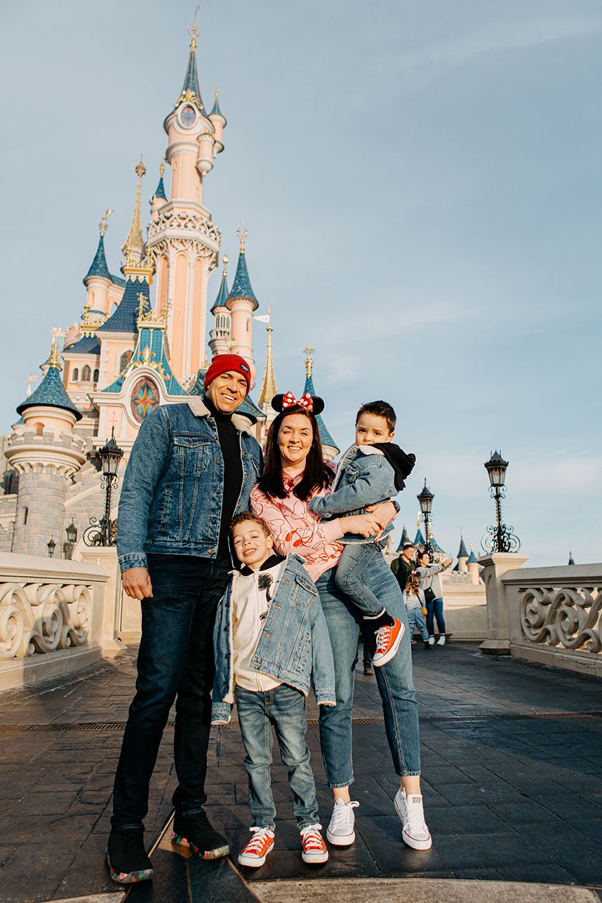 Happy family of four posing in front of Disneyland Paris castle on a sunny day.