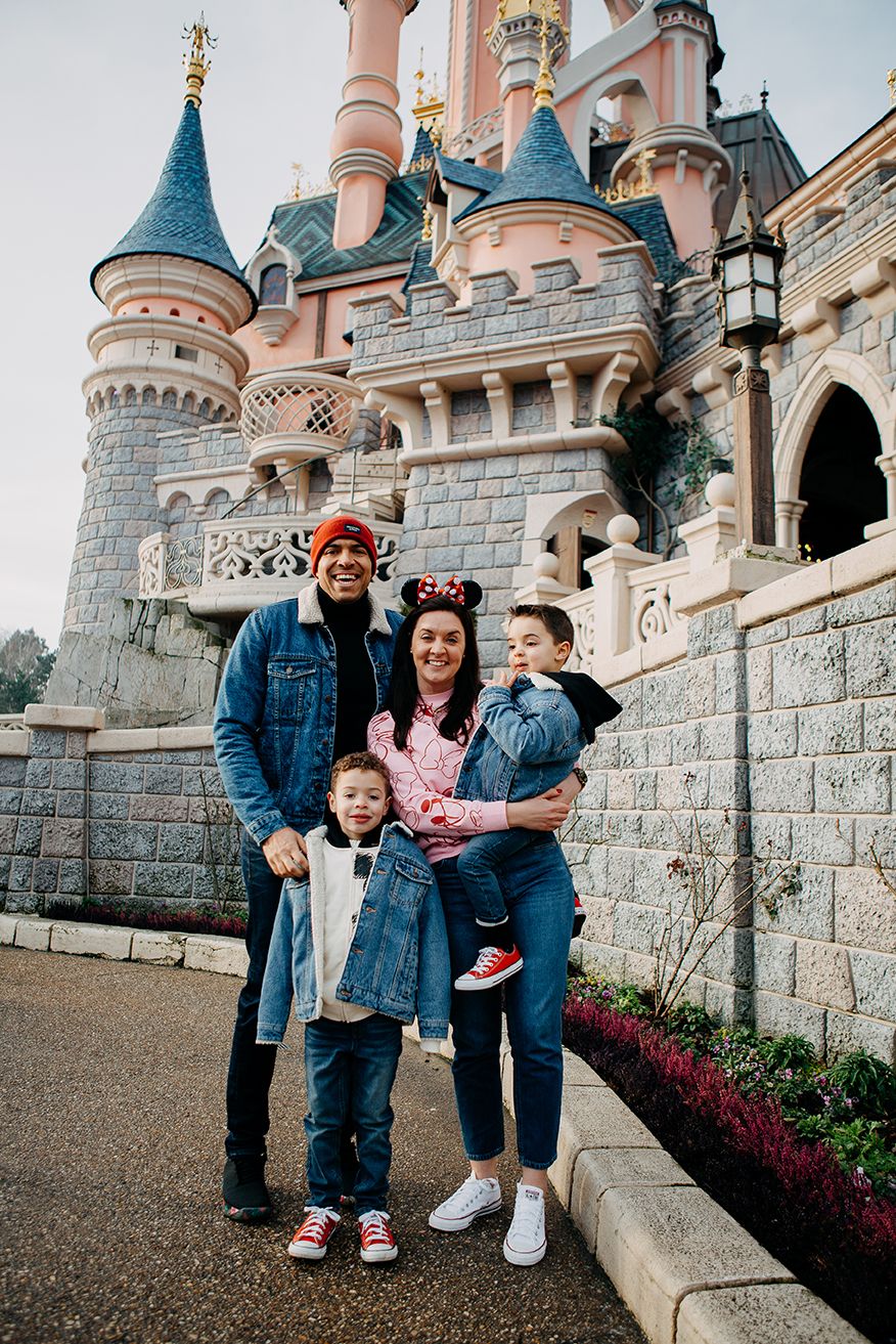 Family of four smiling together beside the iconic Sleeping Beauty Castle at Disneyland Paris.
