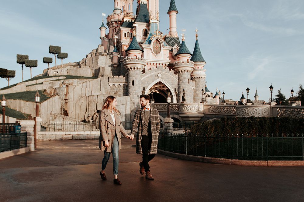 Couple holding hands and strolling in front of Sleeping Beauty Castle at Disneyland Paris.