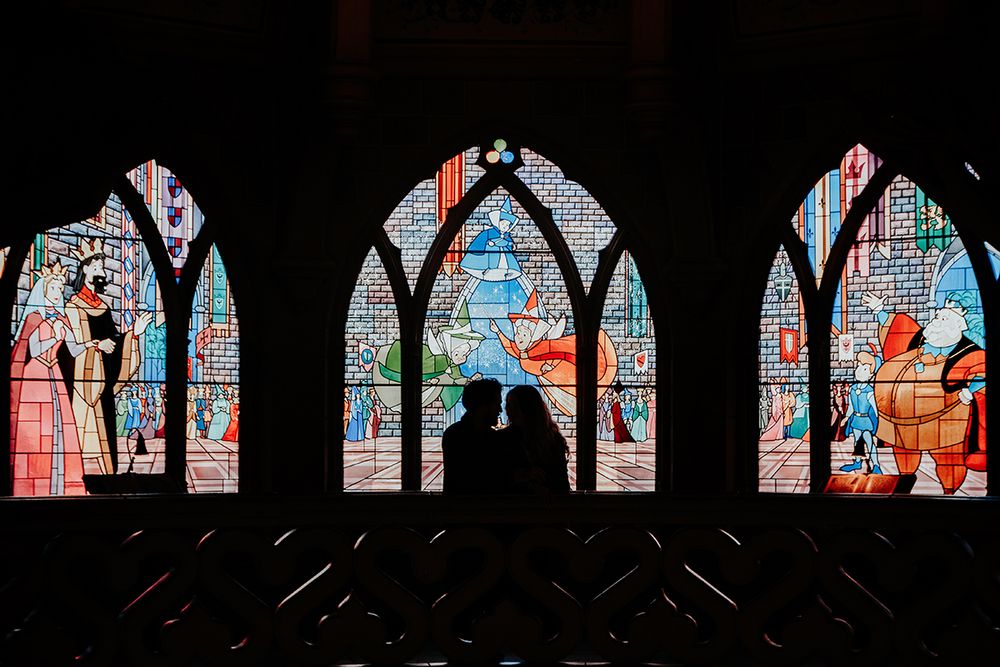 Romantic couple silhouetted against colorful stained glass windows inside Disneyland castle.