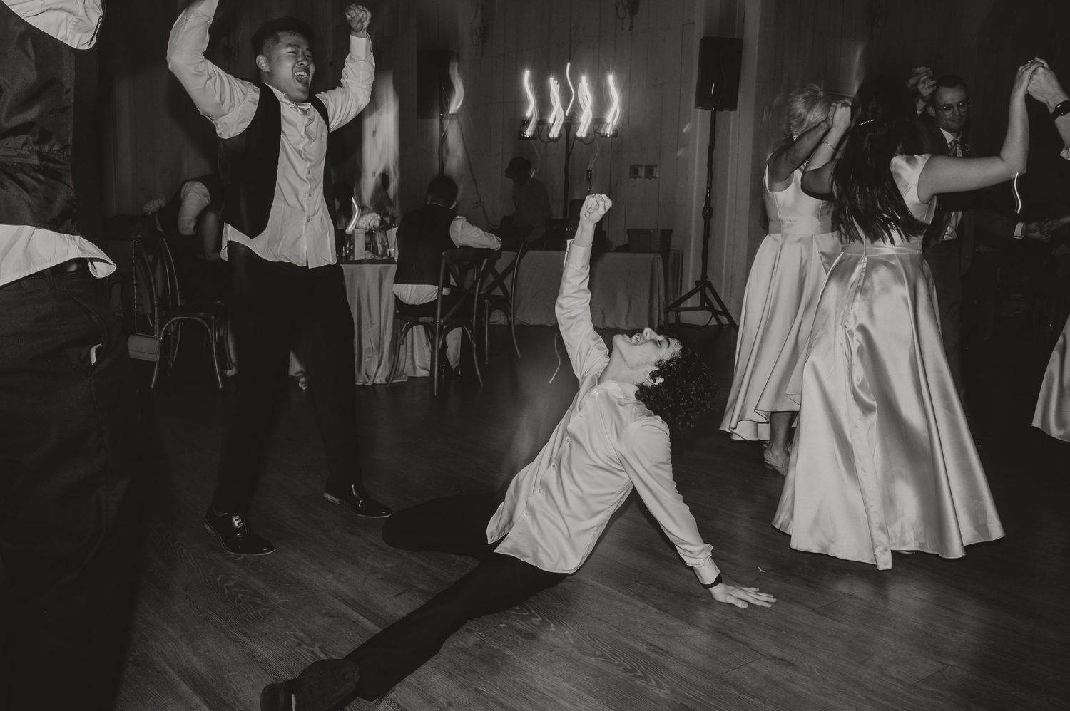Energetic wedding reception dance party in black and white showing guests dancing enthusiastically on a wooden floor.