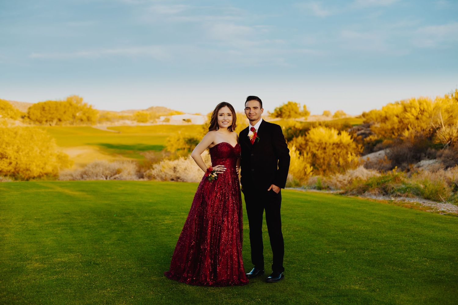 Formal couple poses on golf course with desert mountains in golden sunset light.