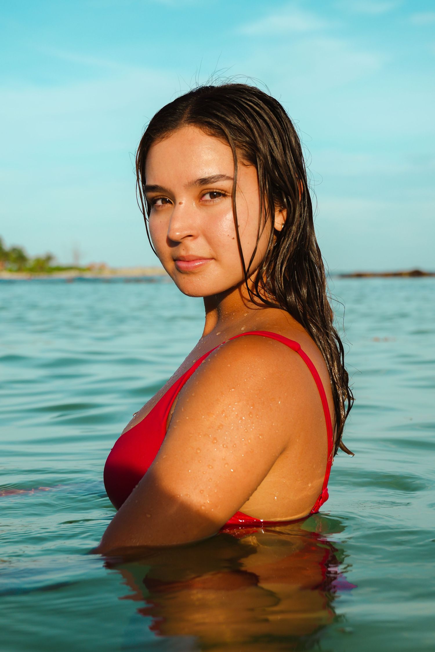Portrait in red swimwear with wet hair against turquoise ocean background.