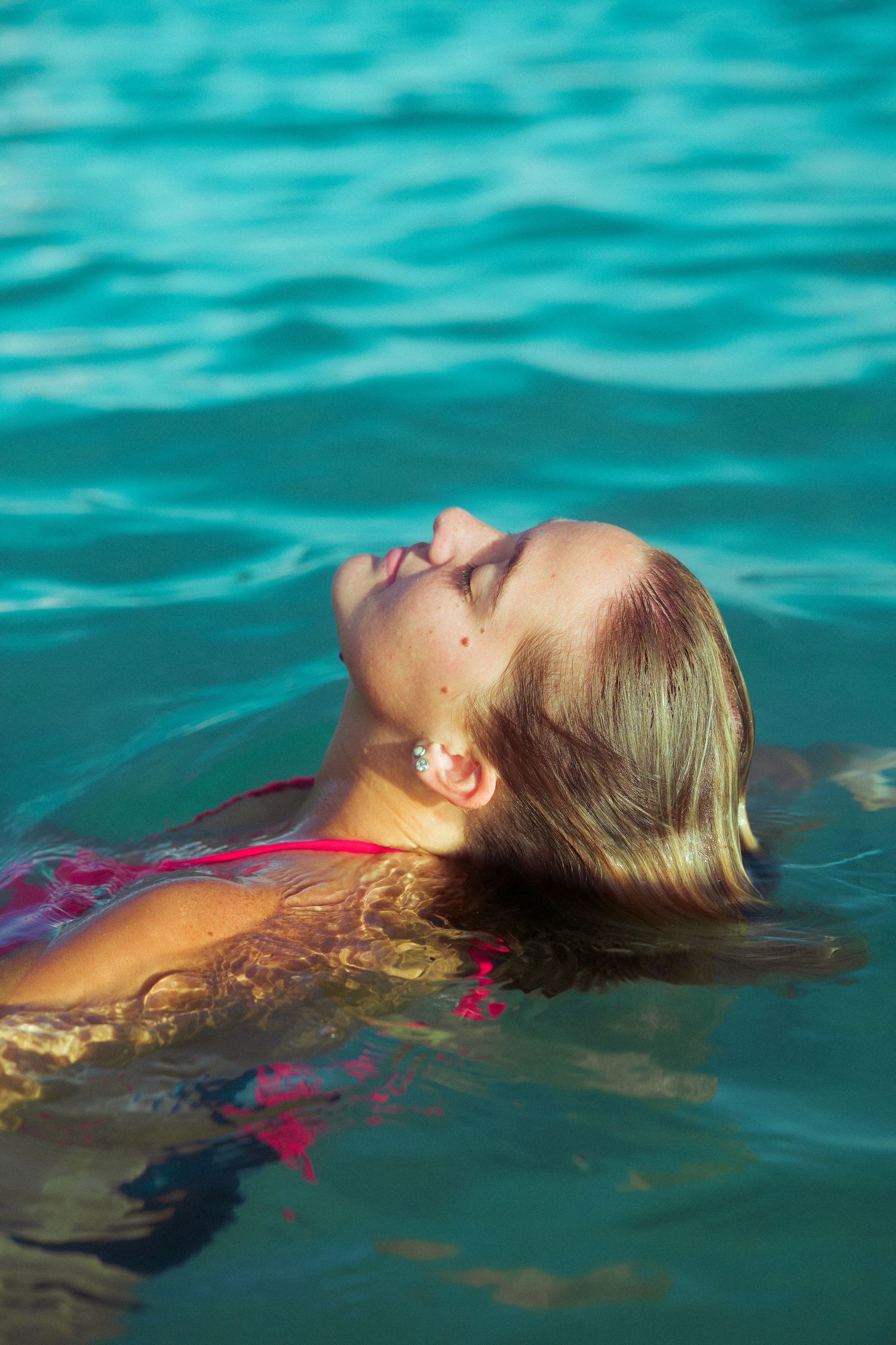 Person floating serenely in turquoise ocean water wearing a red swimsuit on a sunny day.