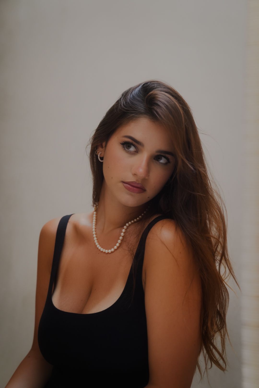 Romantic indoor portrait featuring black tank top and pearl jewelry.