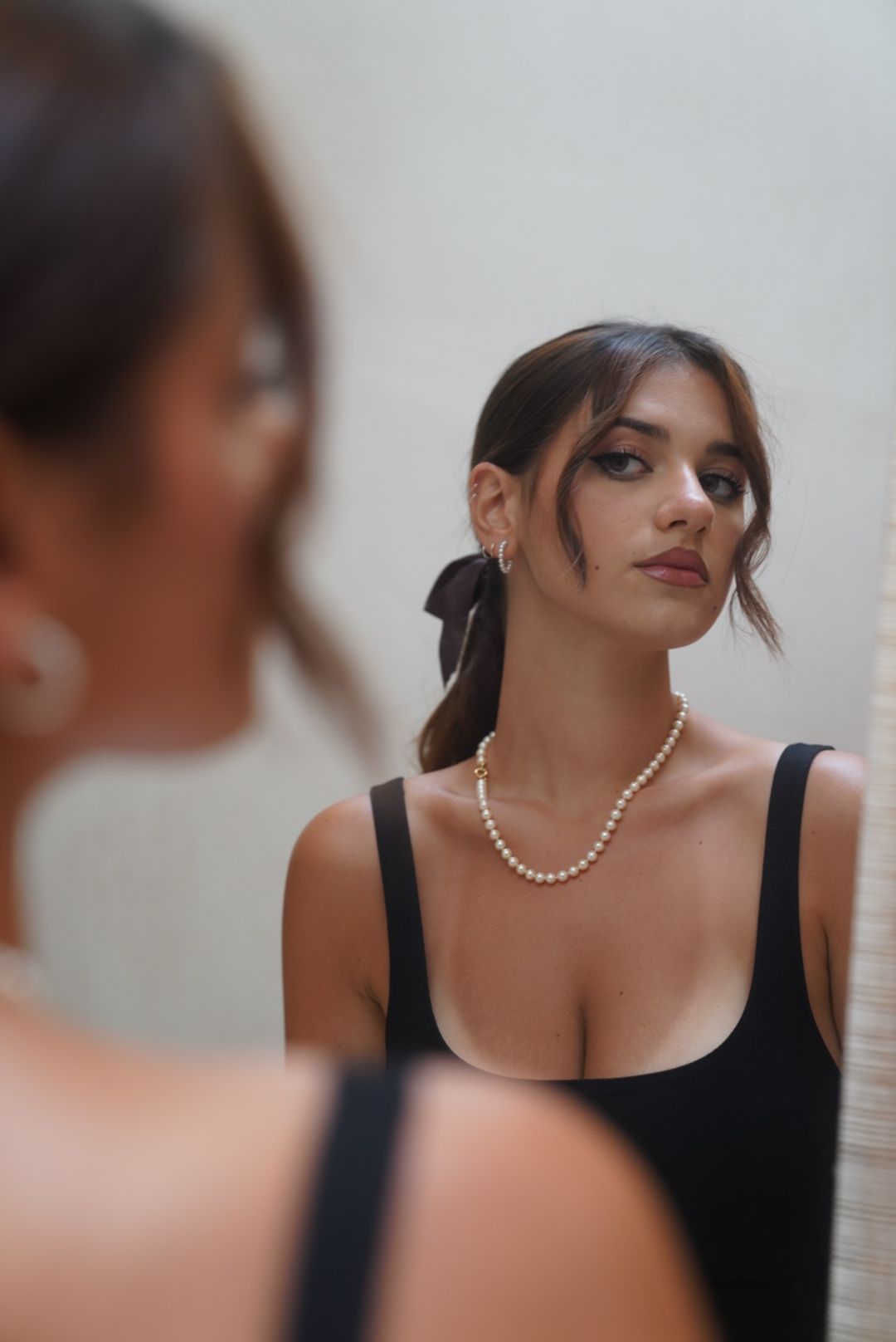 Elegant portrait featuring a black tank top and pearl necklace against a light background.