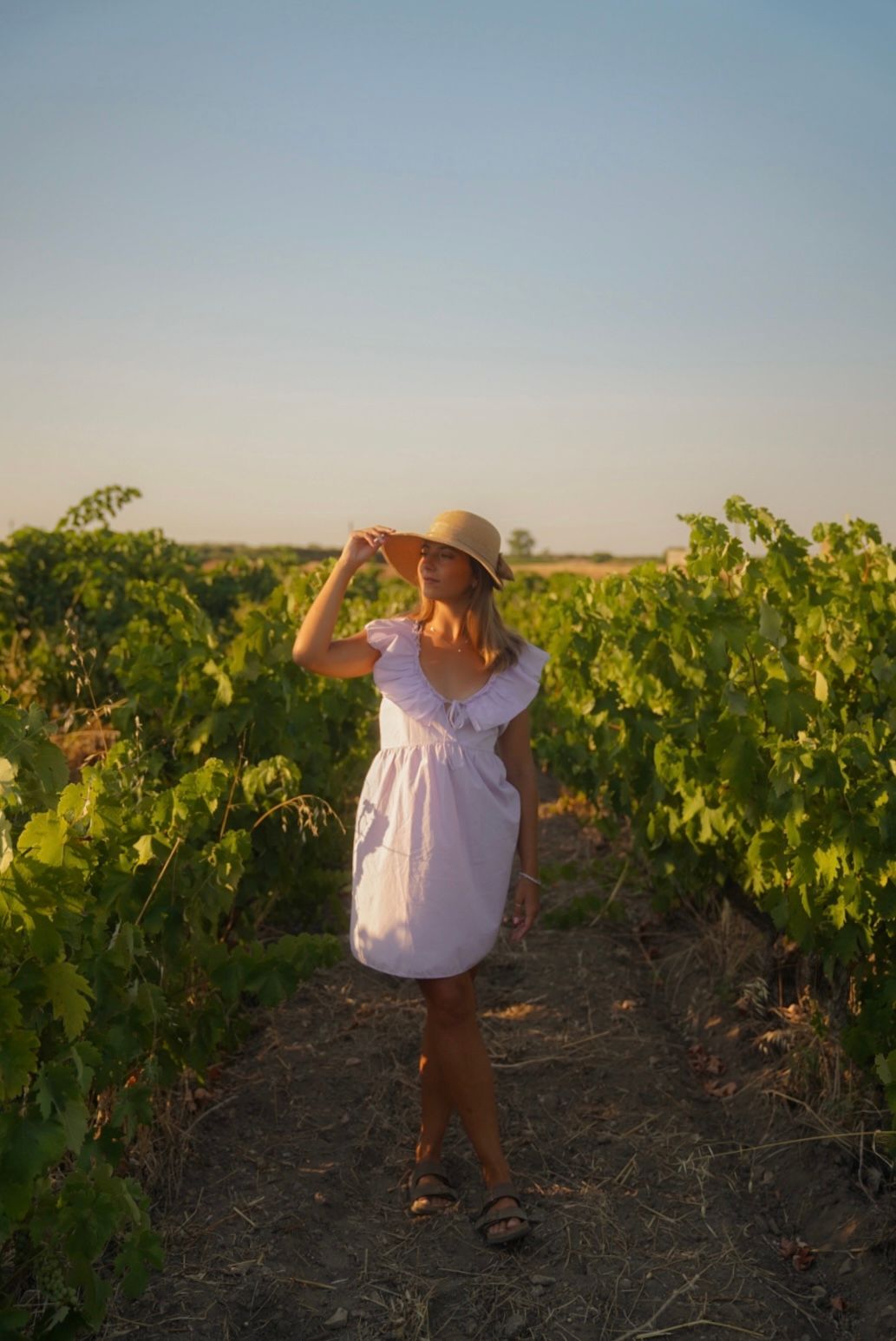 Summer fashion shoot in vineyard featuring white dress and wide-brim hat.