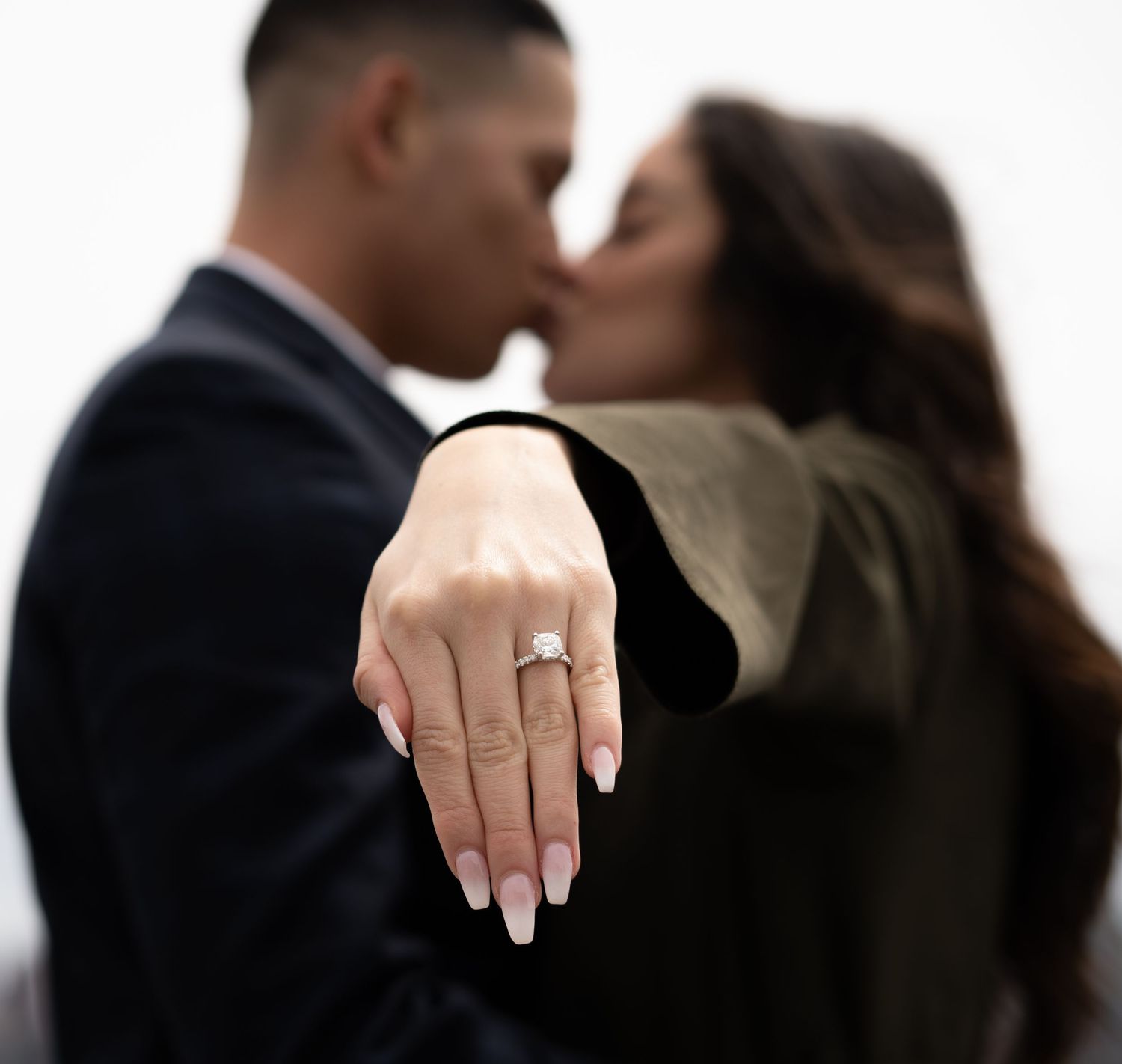 Close-up of hands showing an engagement ring against a white background.