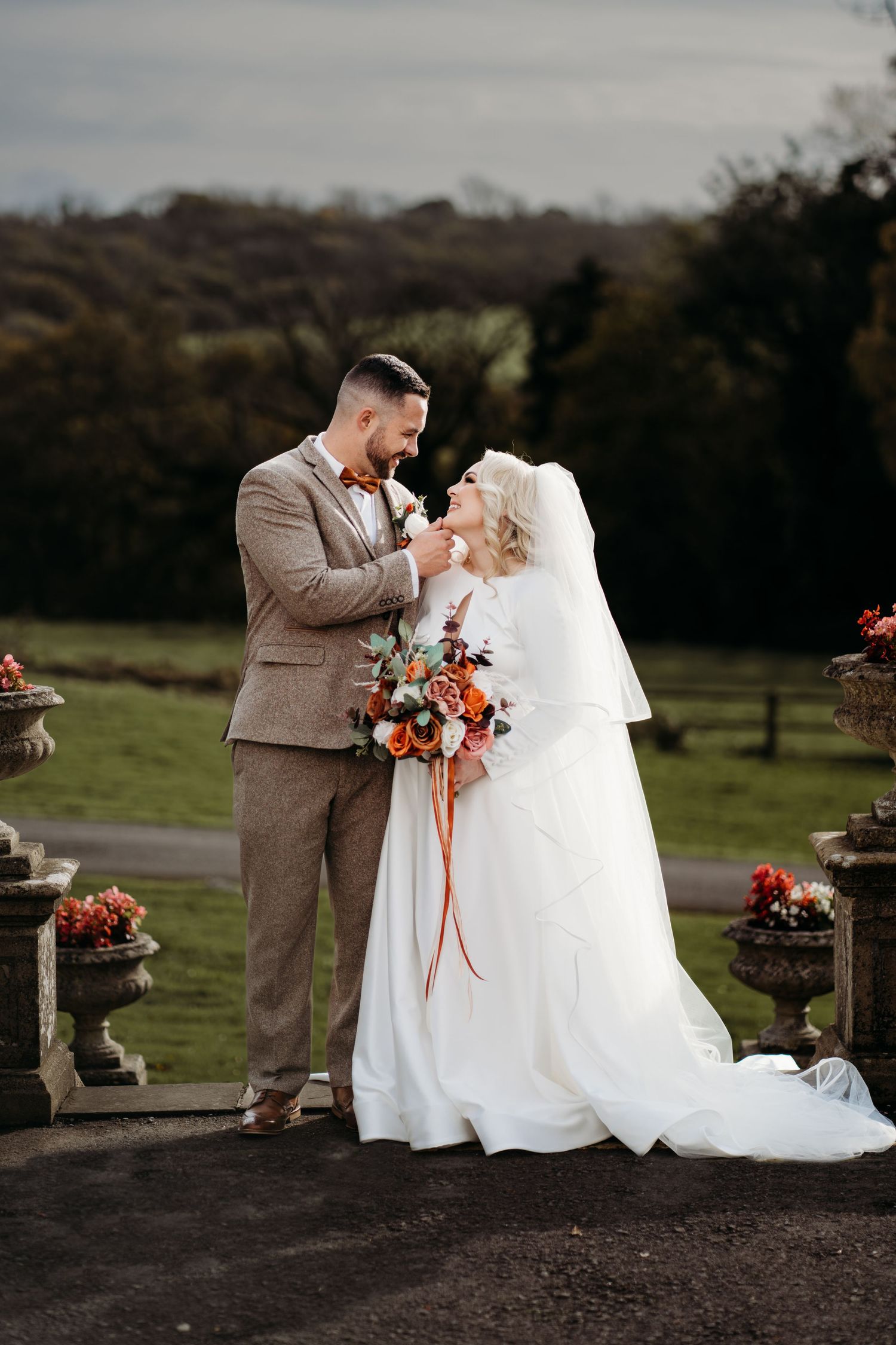 Romantic wedding portrait of couple with autumn floral bouquet at rustic outdoor venue.