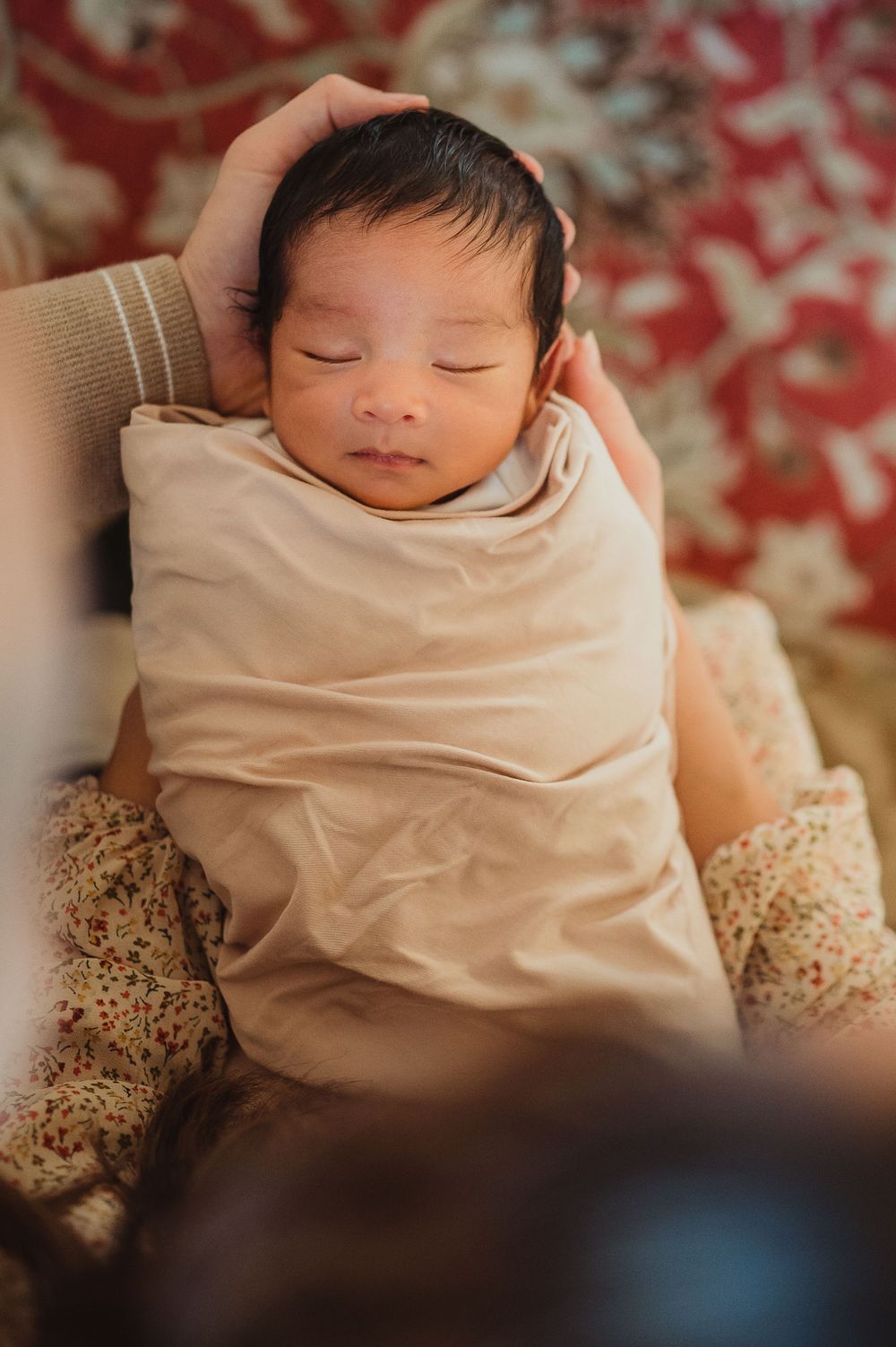 Newborn baby laying on his back, sleeping with a cream colored blanket.