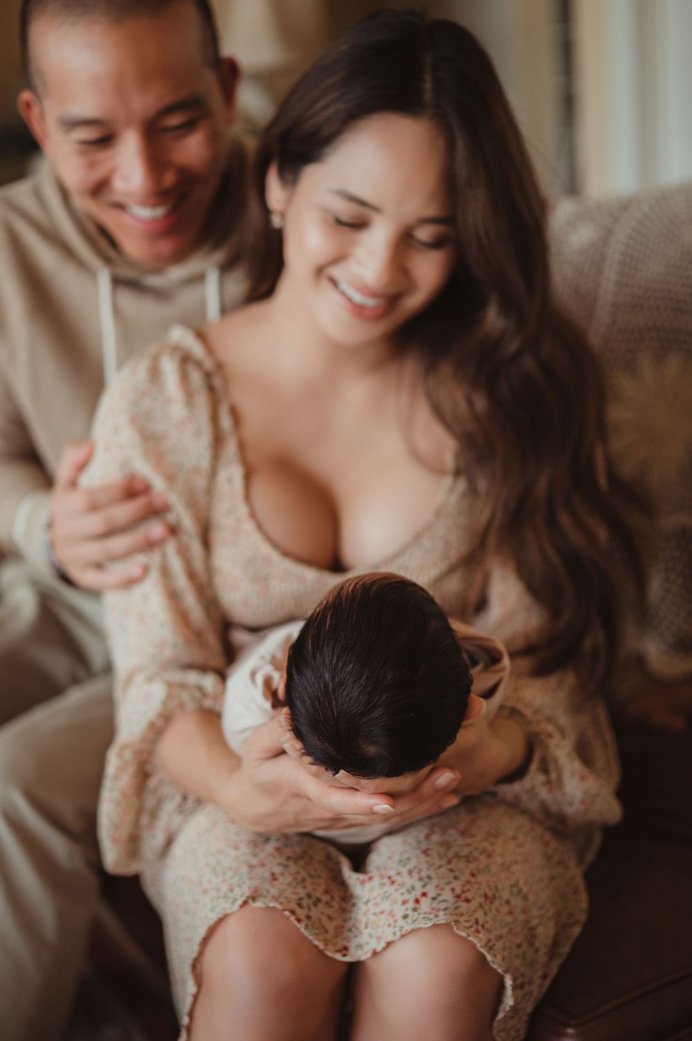 Mom and dad holding their newborn baby sitting on a couch in their house.