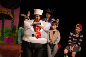 Theater cast members perform scene with snowman character on decorated stage.