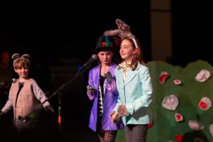 Stage performers sing during a theatrical production with whimsical scenery.