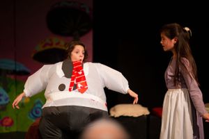 Stage performers in white costumes act during a theatrical production.