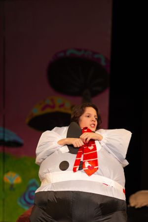 Actor in white snowman costume performs on stage with pink background lighting.