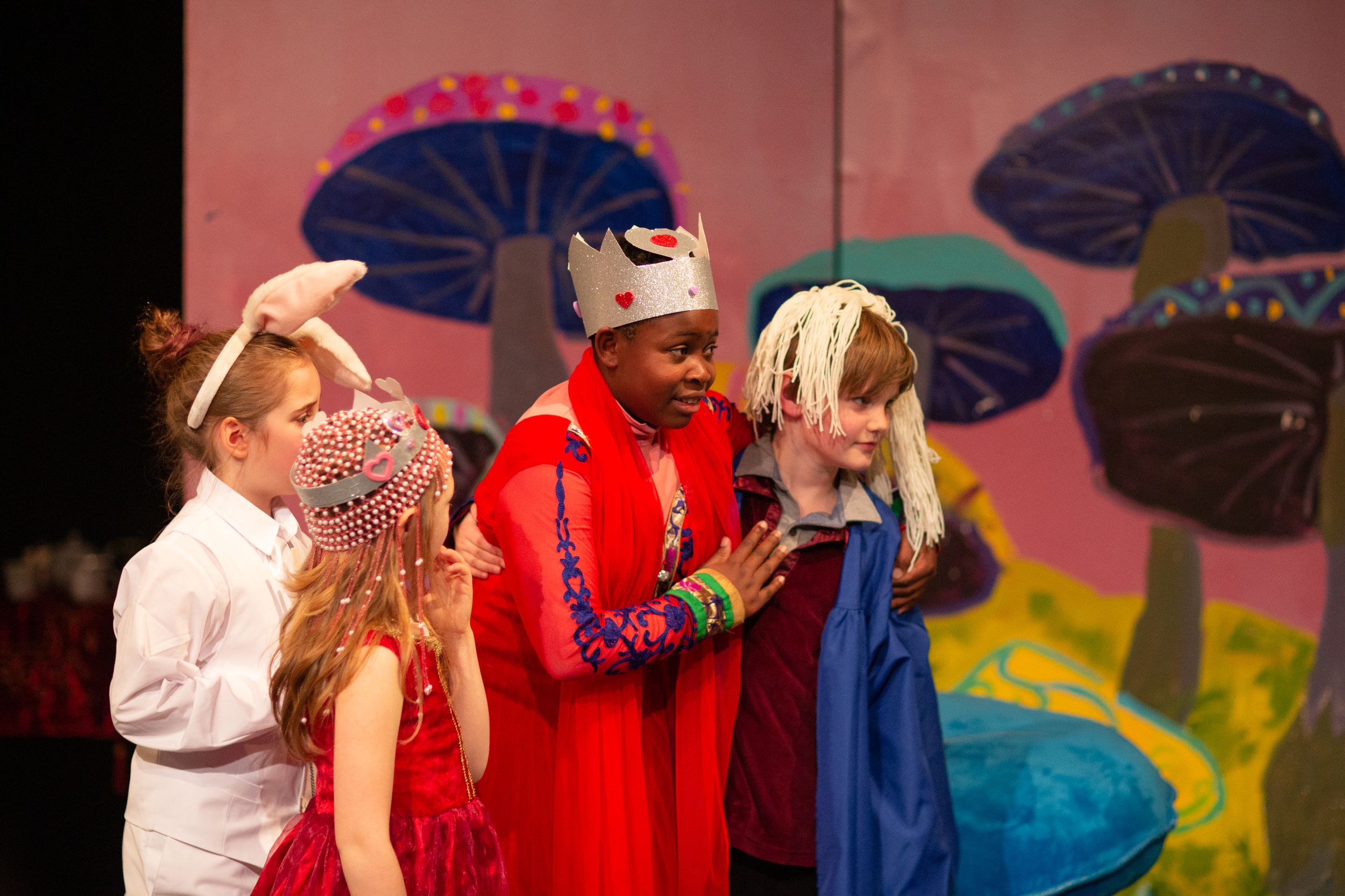 Stage production features colorful mushroom backdrop and performers in vibrant costumes.