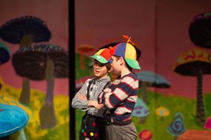 Children perform on stage in colorful costumes during a theatrical production with whimsical scenery.
