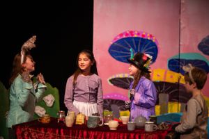 Theater scene with performers gathered around a table against a fantasy mushroom backdrop.