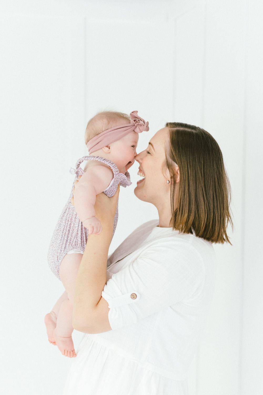 Mother and baby sharing a happy moment against white backdrop.