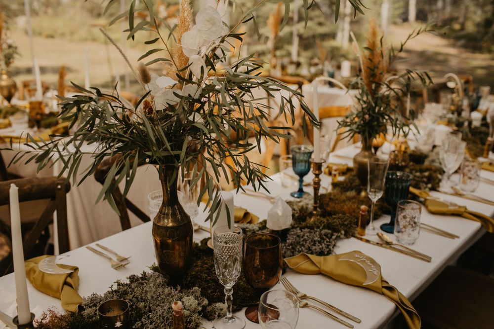 An elegant wedding reception table setting with natural greenery and gold accents.