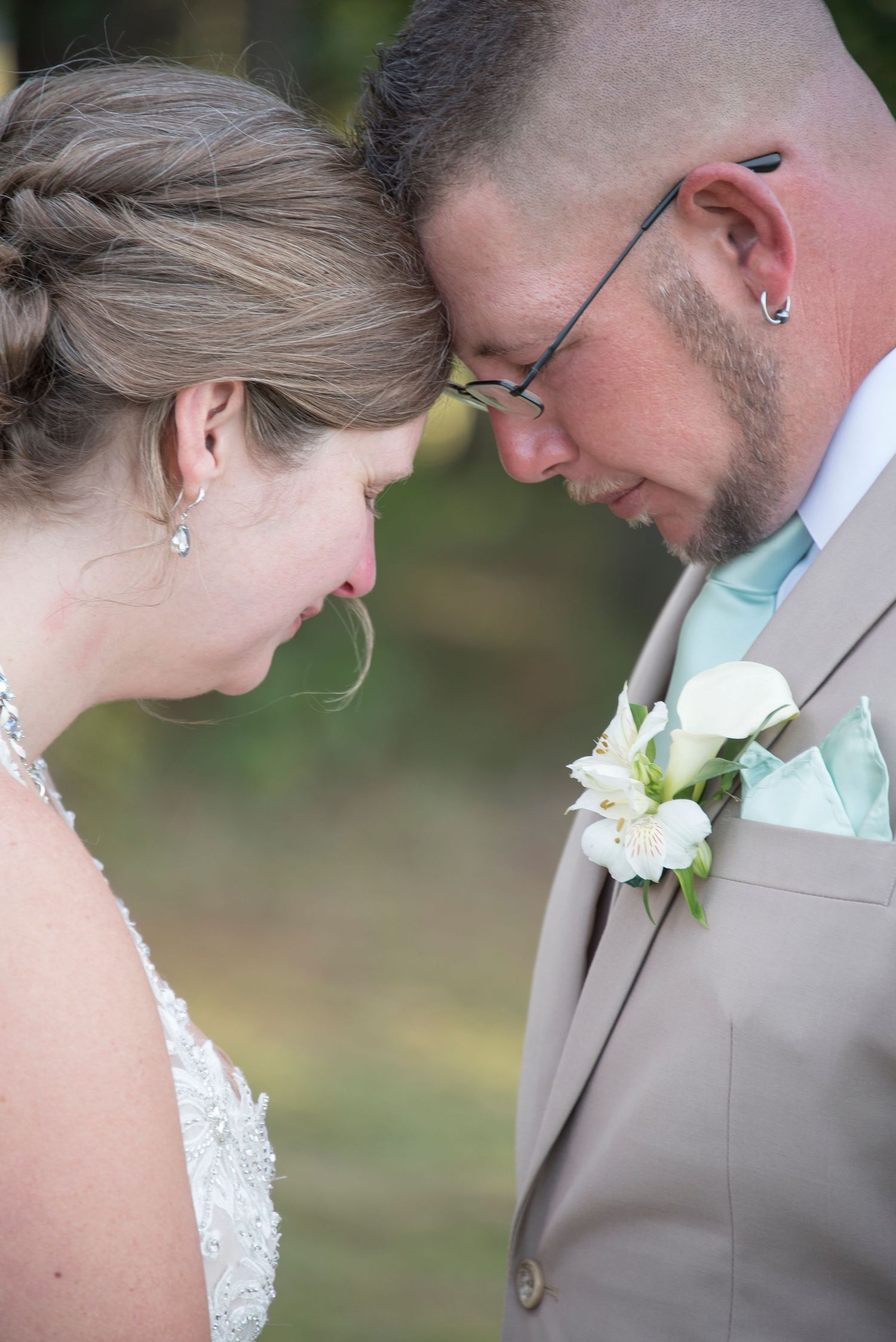 A tender moment between newlyweds wearing wedding attire with a white boutonniere.