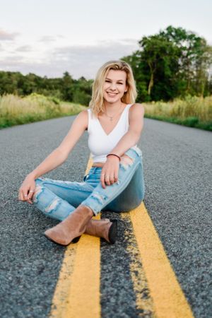 Casual portrait session on asphalt road with yellow lines showing relaxed poses in denim and white top.